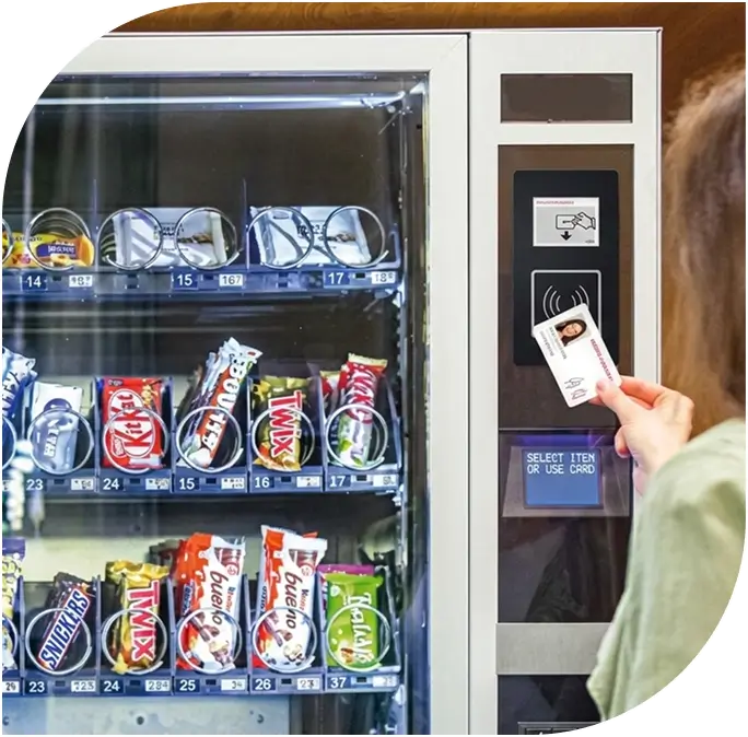 Woman using contactless payment to select an item from a brightly lit vending machine stocked with snacks and drinks, featuring a tap-to-pay card reader and product selection screen, highlighting zero-cost installation and maintenance service in Chicago and suburbs.